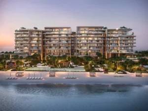Evening beachfront elevation of Alba Residences, Dorchester Collection by OMNIYAT on Palm Jumeirah, highlighting warm architectural lighting, private beach loungers, landscaped gardens, and serene Gulf views. Presented by Tohid Fetrat.
