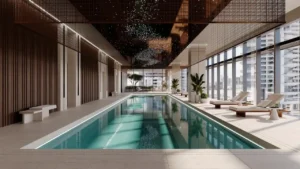 Members club indoor swimming pool at ENARA by OMNIYAT featuring a refined linear pool, lounge seating, floor to ceiling glazing, decorative ceiling panels, and Business Bay city views in Dubai. Presented by Tohid Fetrat.