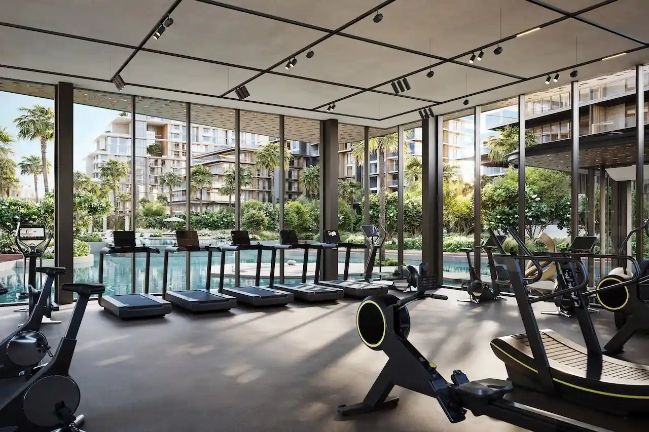 City Walk Crestlane by Meraas showing a luxury gym and fitness center with modern equipment floor to ceiling windows and views of the landscaped lagoon pool and residences presented by Tohid Fetrat.