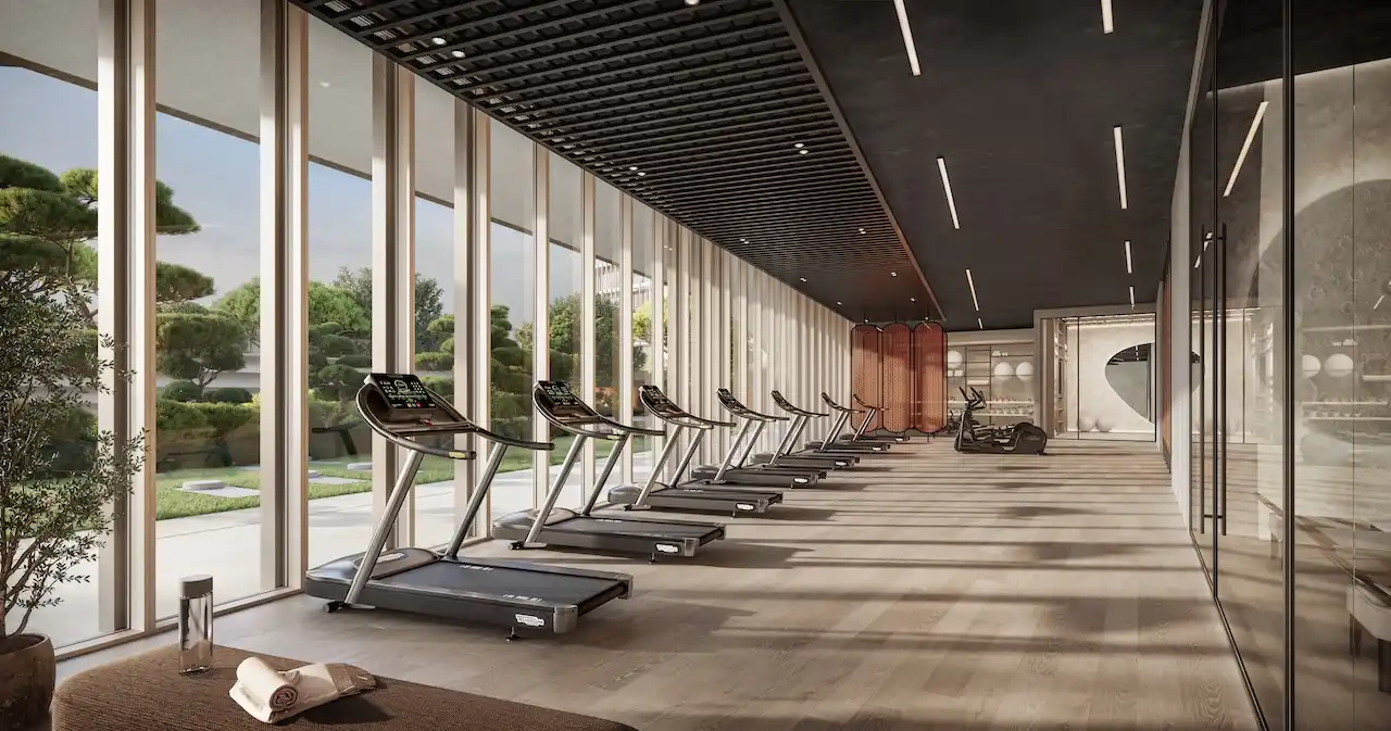 Luxury fitness studio at Hado Tower in the SIORA community by Beyond featuring modern treadmills floor to ceiling windows and serene landscaped garden views presented by Tohid Fetrat.