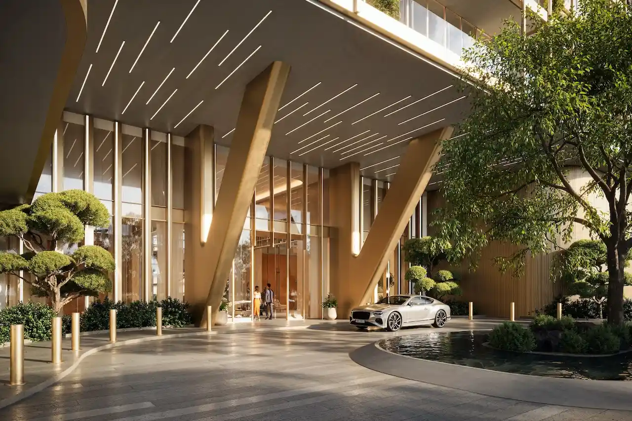 Primary drop off area of Hado Tower in the SIORA community by Beyond featuring grand golden structural columns floor to ceiling glass an elegant arrival driveway landscaped trees and a luxury car presented by Tohid Fetrat.