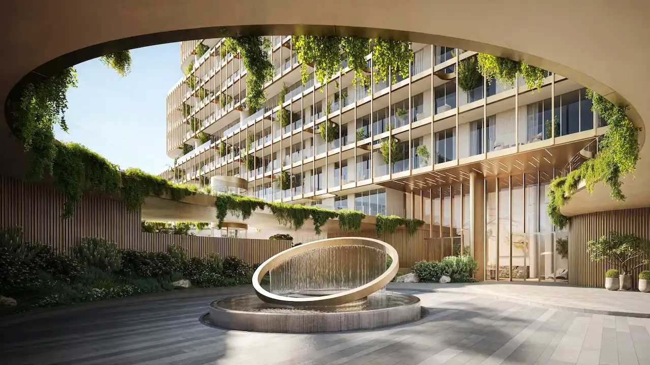 Secondary drop off area of Hado Tower in the SIORA community by Beyond featuring cascading greenery golden architectural detailing a circular water feature and the elegant building facade presented by Tohid Fetrat.