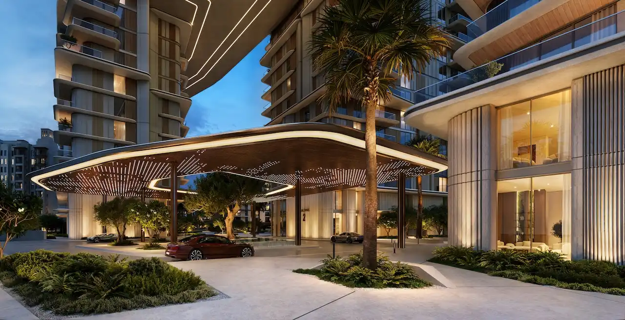 Evening drop off and porte cochere view of MJL Nourelle in Madinat Jumeirah Living Dubai, showcasing sculpted contemporary architecture, warm ambient lighting, palm lined landscaping and a refined luxury residential arrival near the Gulf. Presented by Tohid Fetrat.
