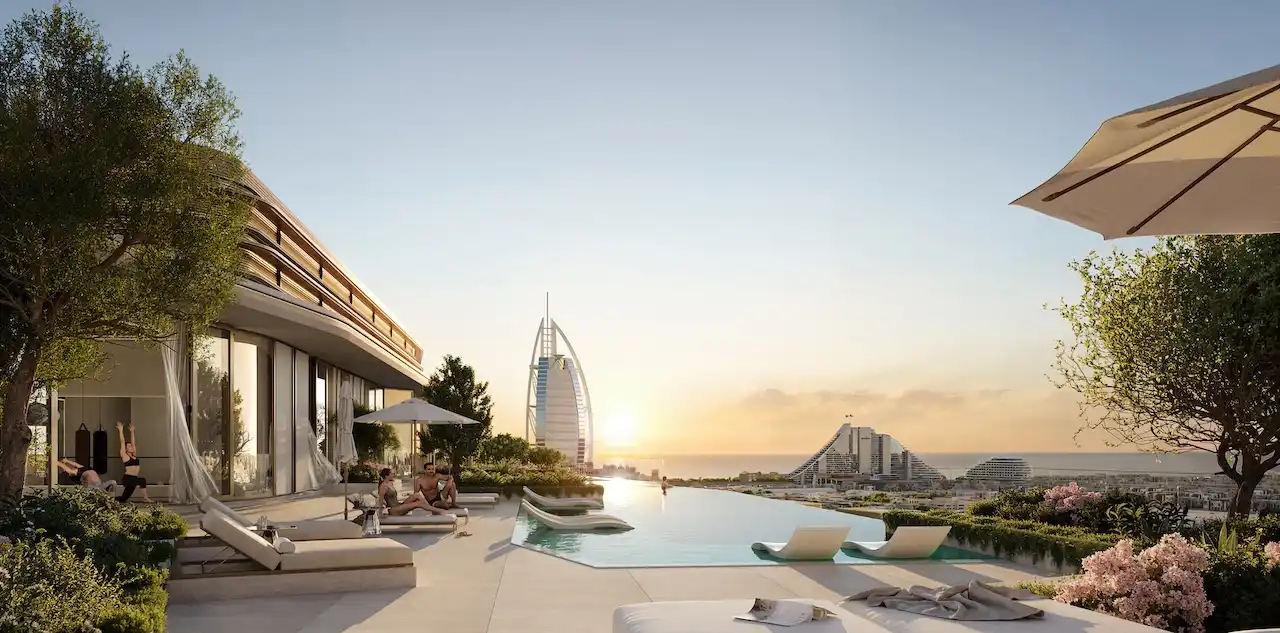 Rooftop infinity pool at MJL Nourelle in Madinat Jumeirah Living Dubai, featuring luxury sun loungers, landscaped terraces and direct views toward Burj Al Arab and the Gulf at sunset. Presented by Tohid Fetrat.