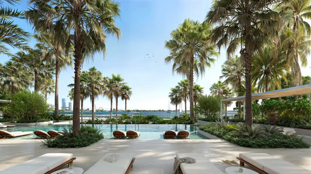 Palm-lined infinity pool at Atelis at d3 featuring resort-style sun loungers, lush tropical landscaping, and serene waterfront views in Dubai Design District. Presented by Tohid Fetrat.