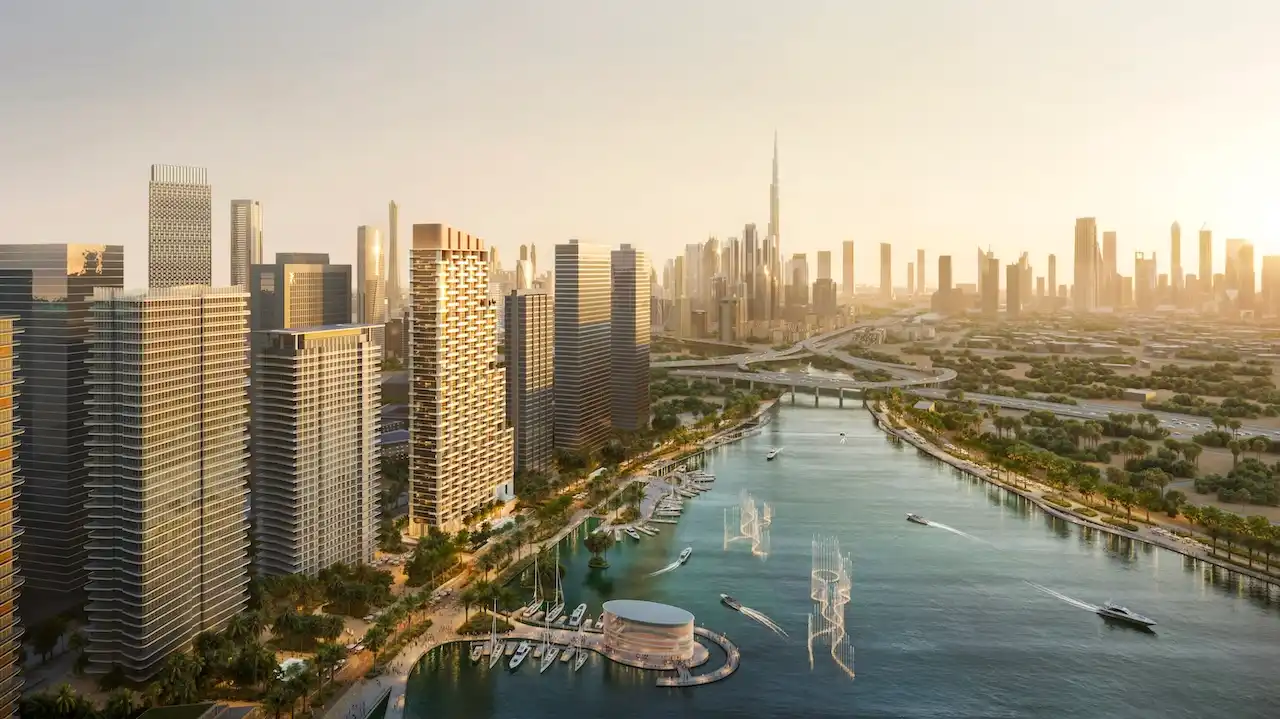 Waterfront exterior view of Atelis at d3 showcasing contemporary residential towers along the canal, with Dubai skyline and Burj Khalifa visible in the background. Presented by Tohid Fetrat.