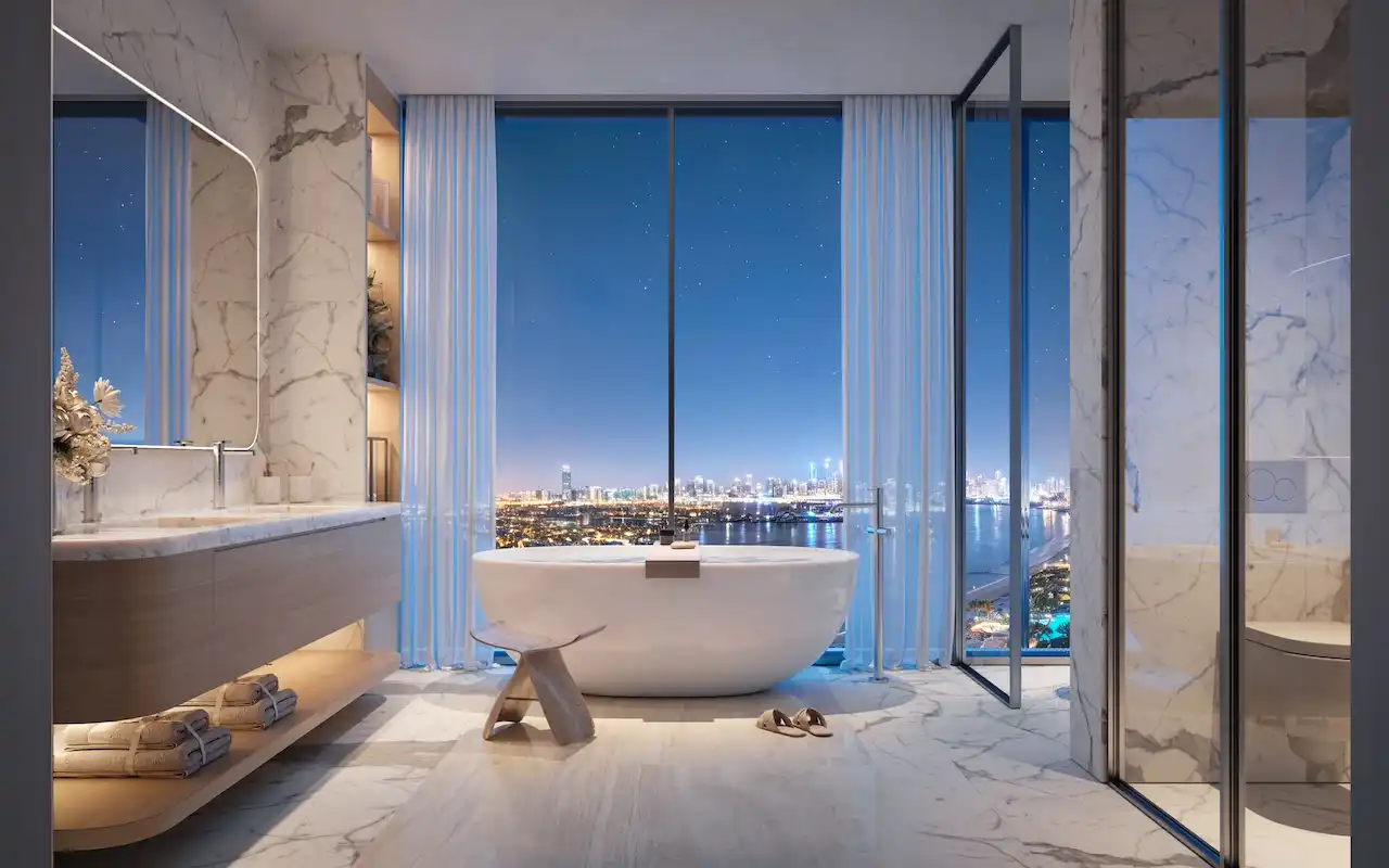 Penthouse master bathroom at Bella at Passo by Beyond featuring a freestanding bathtub, floor-to-ceiling windows, marble finishes, refined contemporary design, and panoramic night views over Palm Jumeirah and the Dubai skyline, Presented by Tohid Fetrat