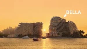 Sunset waterfront view of Bella at Passo by Beyond on Palm Jumeirah featuring stepped contemporary architecture, illuminated façades, palm lined shoreline, anchored boats, and calm coastal waters in Dubai. Presented by Tohid Fetrat.