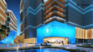 Exterior arrival view of Chelsea Residences featuring a striking blue architectural facade with Chelsea Football Club branding, illuminated podium design, and landscaped entrance plaza in Dubai, Presented by Tohid Fetrat