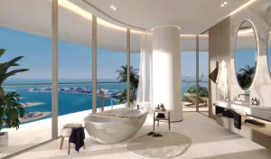 Luxury bathroom interior at COMO Residences on Palm Jumeirah featuring a freestanding marble bathtub, floor-to-ceiling glass walls, refined finishes, and panoramic daytime views of the Gulf and Dubai skyline. Presented by Tohid Fetrat.