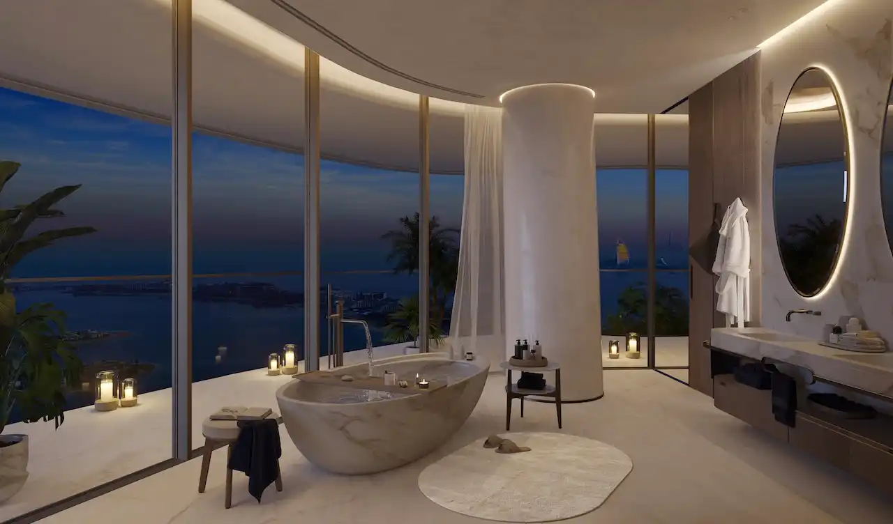 Luxury bathroom interior at COMO Residences on Palm Jumeirah featuring a freestanding marble bathtub, floor-to-ceiling glass walls, refined finishes, and panoramic night views of the Gulf and Dubai skyline. Presented by Tohid Fetrat.
