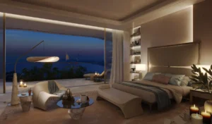 Luxury bedroom at COMO Residences on Palm Jumeirah at night featuring soft ambient lighting, floor-to-ceiling glass, elegant furnishings, and panoramic Gulf and Dubai skyline views. Presented by Tohid Fetrat.