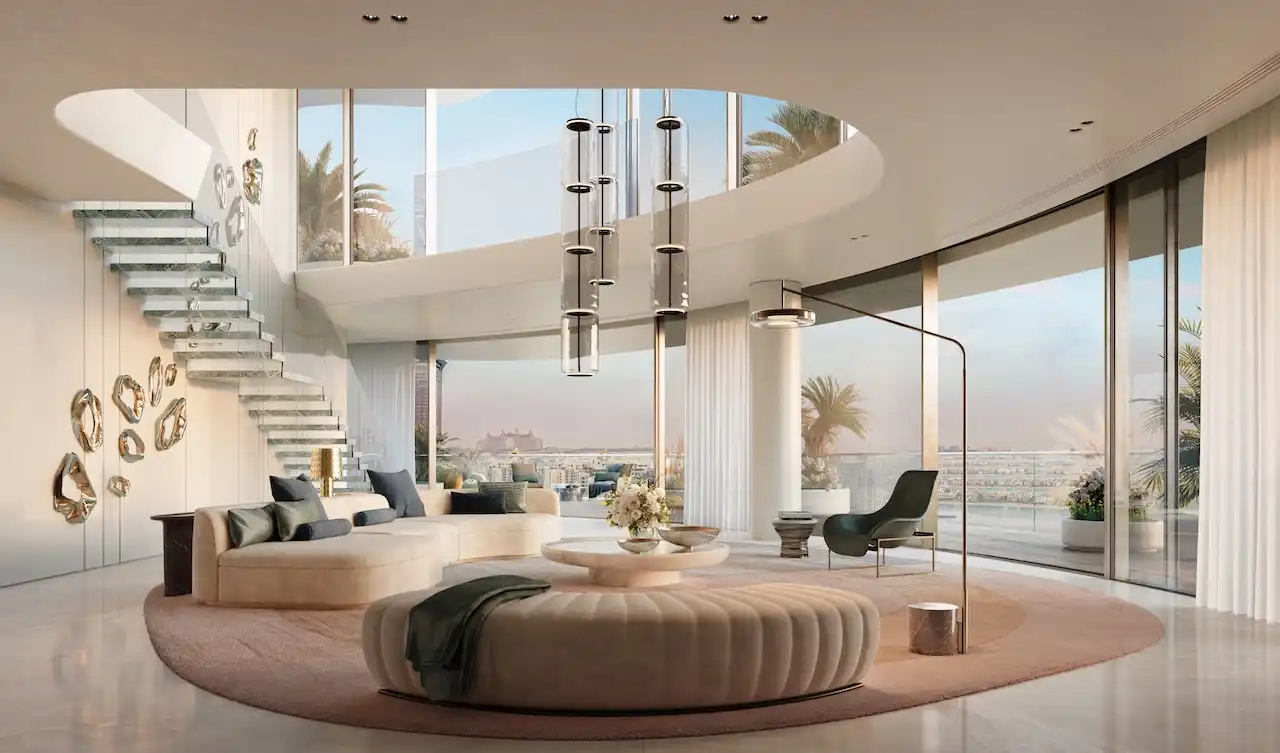 Double-height ultra-luxury living room at COMO Residences on Palm Jumeirah featuring a sculptural floating staircase, statement pendant lighting, bespoke seating, and floor-to-ceiling curved glass with panoramic Gulf views. Presented by Tohid Fetrat.