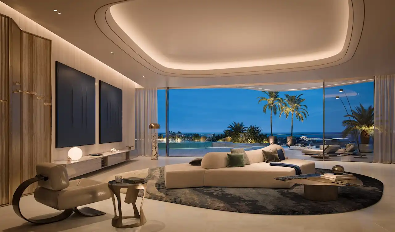 Ultra-luxury living room at COMO Residences on Palm Jumeirah featuring sculptural designer seating, curated wall art, ambient ceiling lighting, and floor-to-ceiling glass opening to a private terrace with Gulf views at night. Presented by Tohid Fetrat.