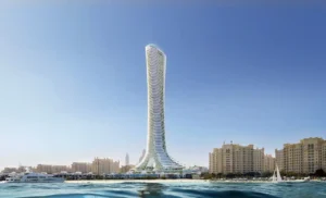 Sea level view of COMO Residences tower rising from the Palm Jumeirah waterfront, showcasing its slender sculpted architecture, beachfront setting, surrounding marina waters, and clear Dubai skyline backdrop. Presented by Tohid Fetrat.