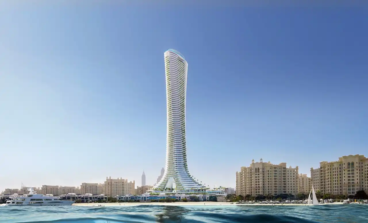 Sea level view of COMO Residences tower rising from the Palm Jumeirah waterfront, showcasing its slender sculpted architecture, beachfront setting, surrounding marina waters, and clear Dubai skyline backdrop. Presented by Tohid Fetrat.