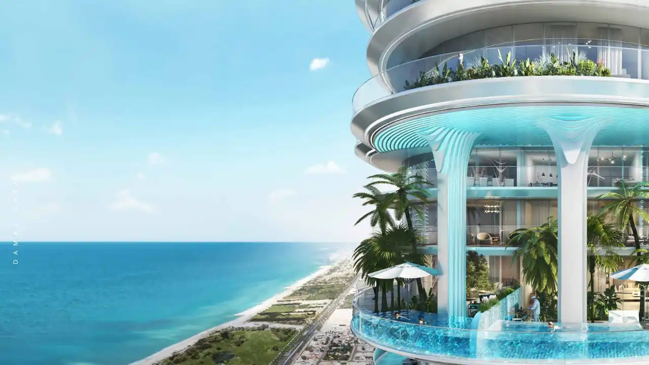 DAMAC Casa ocean-view sky pool terrace featuring sculptural waterfall columns, curved glass balconies, and lush tropical landscaping overlooking the Gulf coastline in Dubai. Presented by Tohid Fetrat.