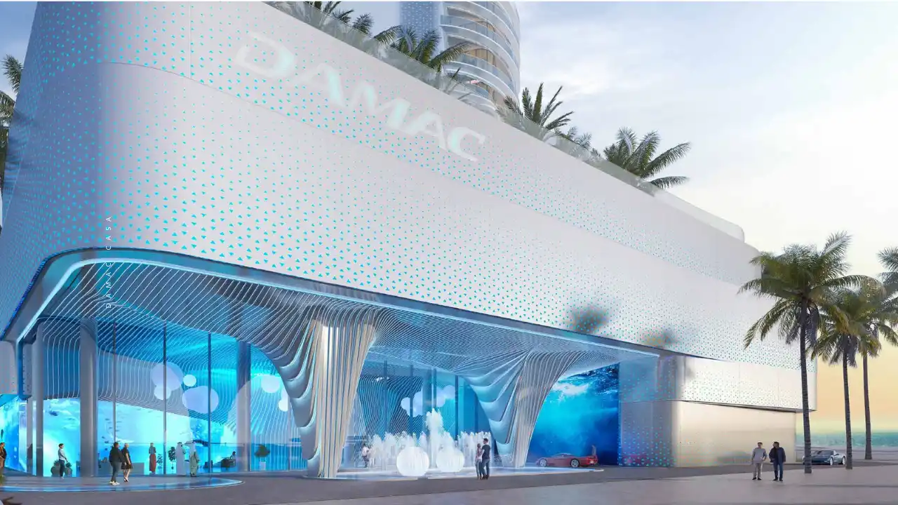 DAMAC Casa podium entrance featuring a sculpted architectural façade with illuminated patterns, double-height retail and lobby spaces, and contemporary waterfront design in Dubai. Presented by Tohid Fetrat.