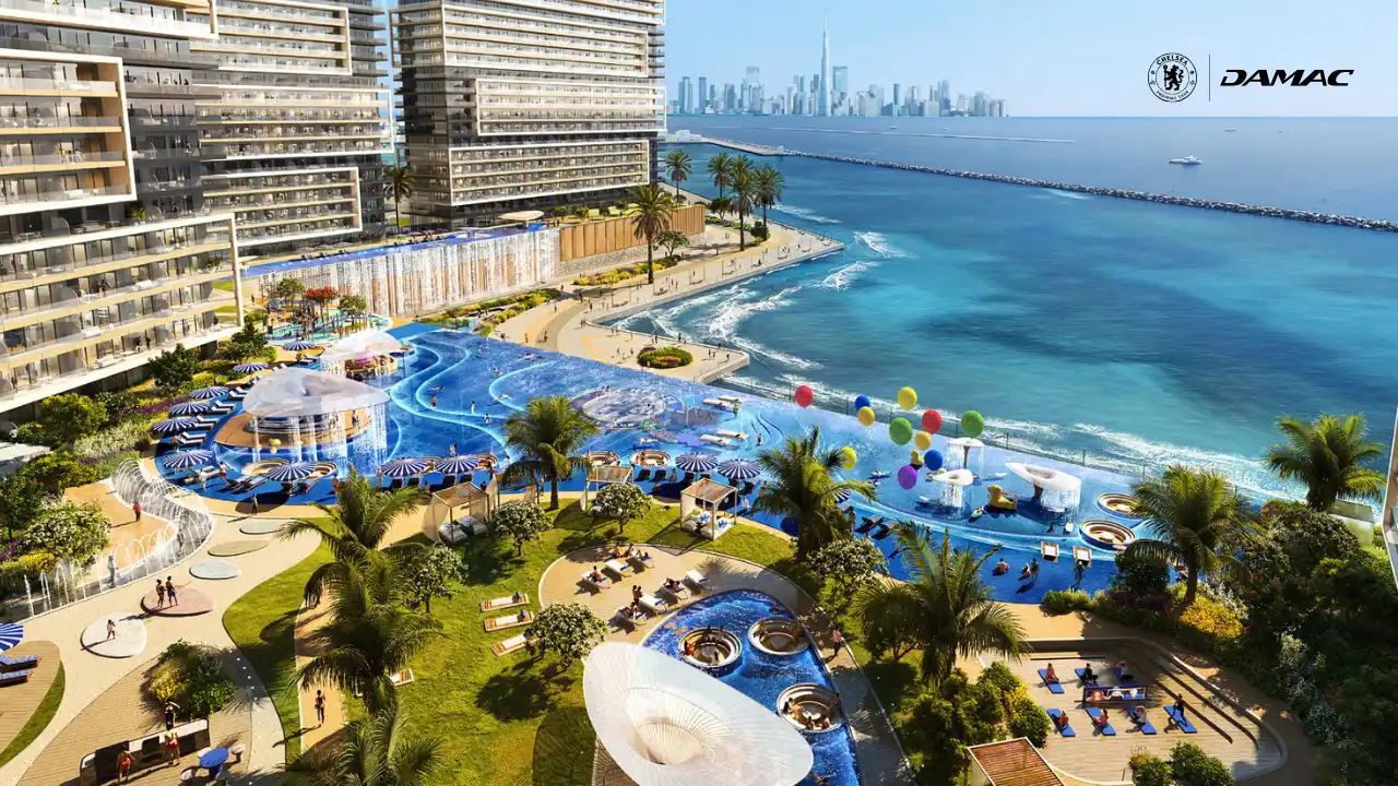 Aerial view of the infinity beach pool at DAMAC Chelsea Residences featuring expansive blue pools, palm lined leisure decks, cabanas, and direct waterfront views across the Gulf in Dubai, Presented by Tohid Fetrat