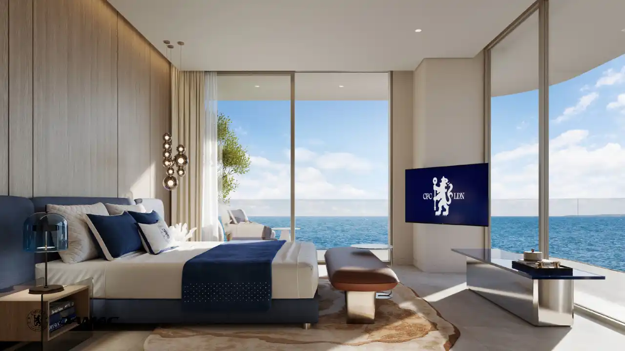 Interior view of the master bedroom at DAMAC Chelsea Residences featuring a refined bed setting, soft blue accents, floor to ceiling windows, and open sea views in Dubai, Presented by Tohid Fetrat