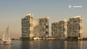 Waterfront exterior view of DAMAC Chelsea Residences featuring contemporary stepped towers, expansive balconies, Chelsea branding, and a calm coastal setting with open water and skyline views in Dubai, Presented by Tohid Fetrat