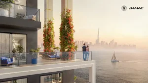 Waterfront terrace at DAMAC Chelsea Residences featuring landscaped columns, glass balustrades, outdoor seating, and expansive views across the water toward the Dubai skyline at sunset, Presented by Tohid Fetrat