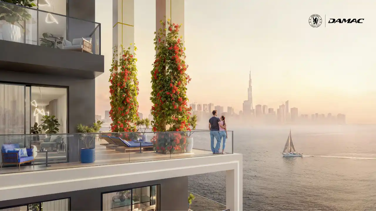 Waterfront terrace at DAMAC Chelsea Residences featuring landscaped columns, glass balustrades, outdoor seating, and expansive views across the water toward the Dubai skyline at sunset, Presented by Tohid Fetrat