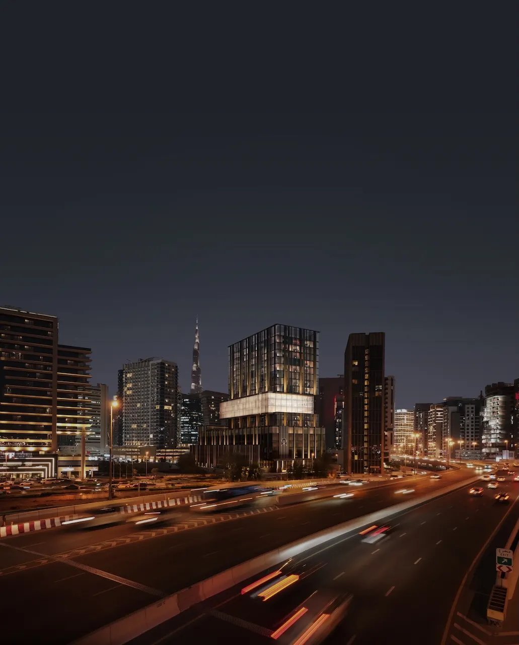 Night aerial view of Haus of Tenet by IRTH in Business Bay, Dubai, showcasing illuminated architecture, Burj Khalifa skyline backdrop, and major highway connectivity, presented by Tohid Fetrat