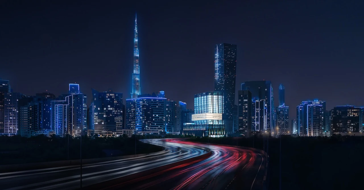 Night skyline view of Haus of Tenet by IRTH in Business Bay, Dubai, with Burj Khalifa in the background, illuminated city towers, and highway light trails highlighting the project’s central urban location, presented by Tohid Fetrat