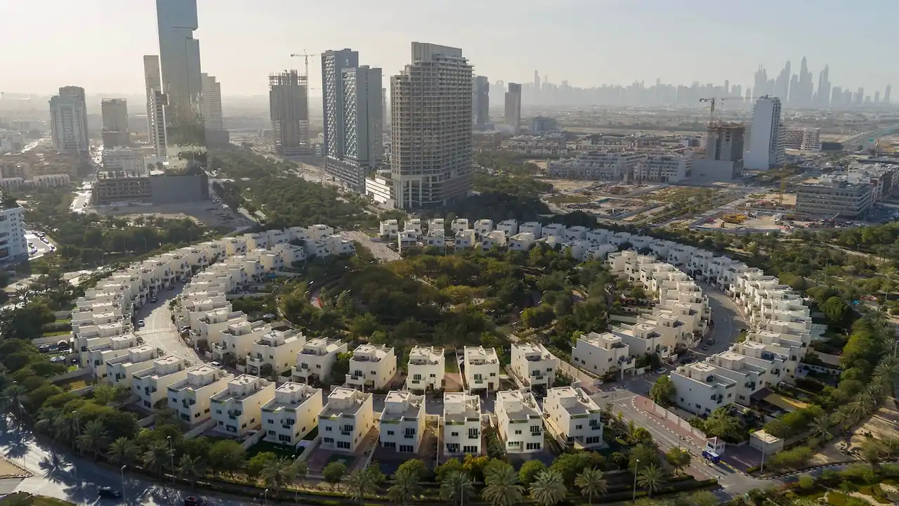 Aerial view of Jumeirah Village Circle (JVC) in Dubai showcasing circular urban planning residential villas green spaces and high-rise buildings with the Dubai skyline in the background. Presented by Tohid Fetrat.