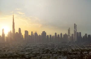 Panoramic sunset view of Dubai’s skyline featuring Burj Khalifa and the distinctive twin towers of Lumena Alta rising on the horizon. Presented by Tohid Fetrat.