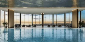 Indoor luxury swimming pool at Lumena Alta featuring floor to ceiling glass walls panoramic city views refined lounge seating and a serene wellness-focused design in Dubai. Presented by Tohid Fetrat.