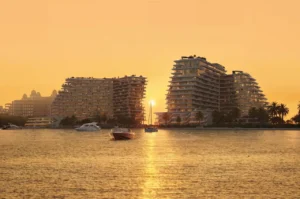 Sunset waterfront view of Passo by Beyond on Palm Jumeirah, featuring luxury residential buildings reflected on calm Gulf waters with yachts and boats creating an iconic Dubai evening skyline. Presented by Tohid Fetrat.