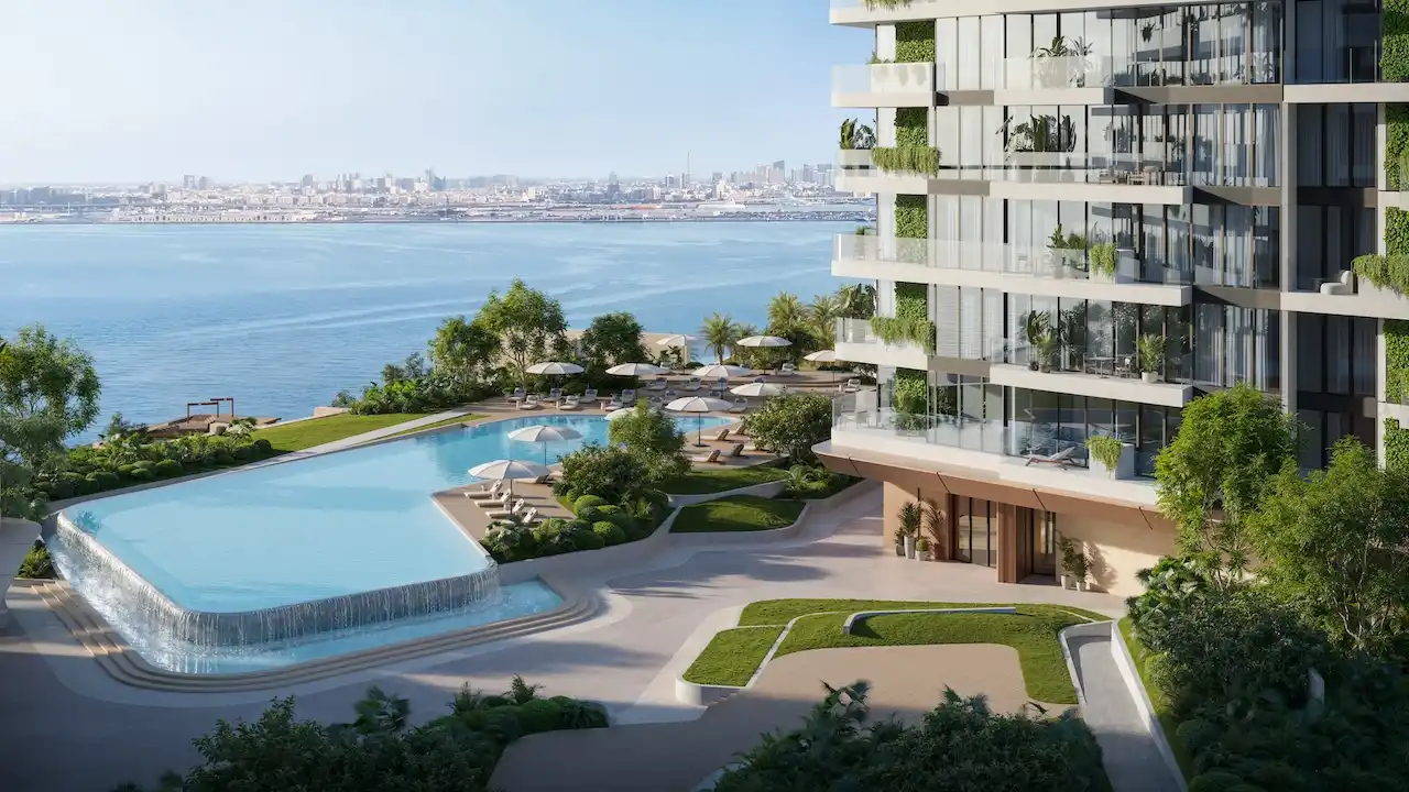 Podium view of Soulever featuring a seafront infinity pool, sun loungers, and landscaped terraces beside luxury residential towers overlooking the Gulf in Dubai. Presented by Tohid Fetrat.