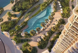 Aerial view of the landscaped lagoon-style swimming pool surrounded by palm trees, sun loungers, and curved pathways between residential towers at The Edit at d3 in Dubai Design District, Presented by Tohid Fetrat