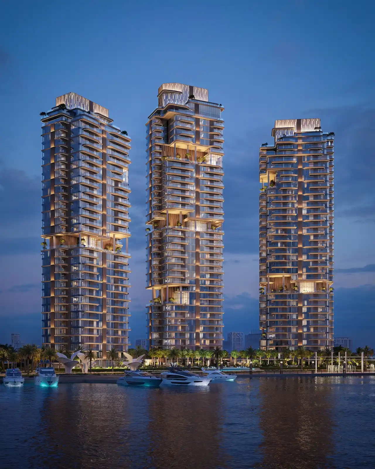 Nighttime waterfront view of the three illuminated residential towers at The Edit at d3 with yachts in the foreground, located in Dubai Design District, Presented by Tohid Fetrat