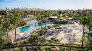 Resort style lagoon pool and outdoor amenities at Nad Al Sheba Gardens Phase 11 with palm trees, lounge areas and Dubai skyline in the background Presented by Tohid Fetrat