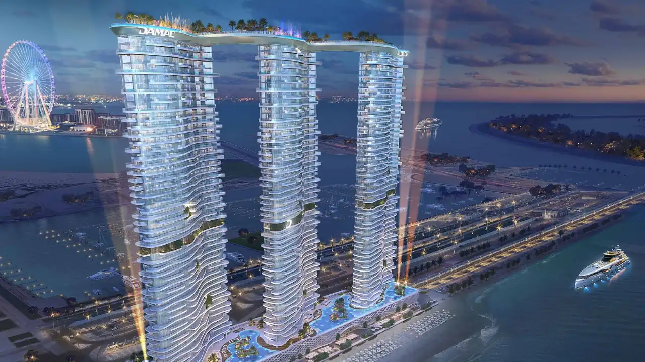 DAMAC Bay by Cavalli illuminated waterfront towers with sky bridge and marina views at night in Dubai - Presented by Tohid Fetrat