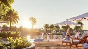 DAMAC Hills 2 by DAMAC Properties lagoon beach at sunset with palm trees sun loungers umbrellas and relaxed outdoor setting in Dubai - Presented by Tohid Fetrat