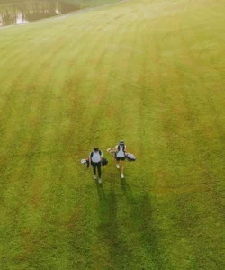 Golf Dale at Emaar South by Emaar golfers walking across green fairway carrying equipment under soft sunlight in Dubai - Presented by Tohid Fetrat