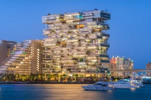 One at Palm Jumeirah Dorchester Collection by Omniyat evening waterfront view with illuminated building and yachts in Dubai - Presented by Tohid Fetrat