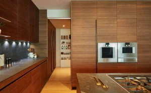 One at Palm Jumeirah Dorchester Collection by Omniyat modern kitchen with wood cabinetry built in appliances and island in Dubai - Presented by Tohid Fetrat