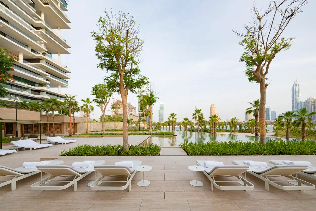 One at Palm Jumeirah Dorchester Collection by Omniyat poolside lounge deck with sunbeds and landscaped views in Dubai - Presented by Tohid Fetrat