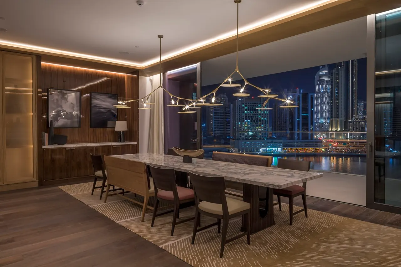 The Lana Residences Dorchester Collection by Omniyat 4 bedroom dining area with city night view and modern chandelier lighting in Dubai - Presented by Tohid Fetrat