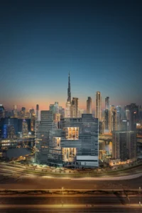 The Lana Residences Dorchester Collection by Omniyat illuminated towers with Downtown Dubai skyline and Burj Khalifa at night in Dubai - Presented by Tohid Fetrat