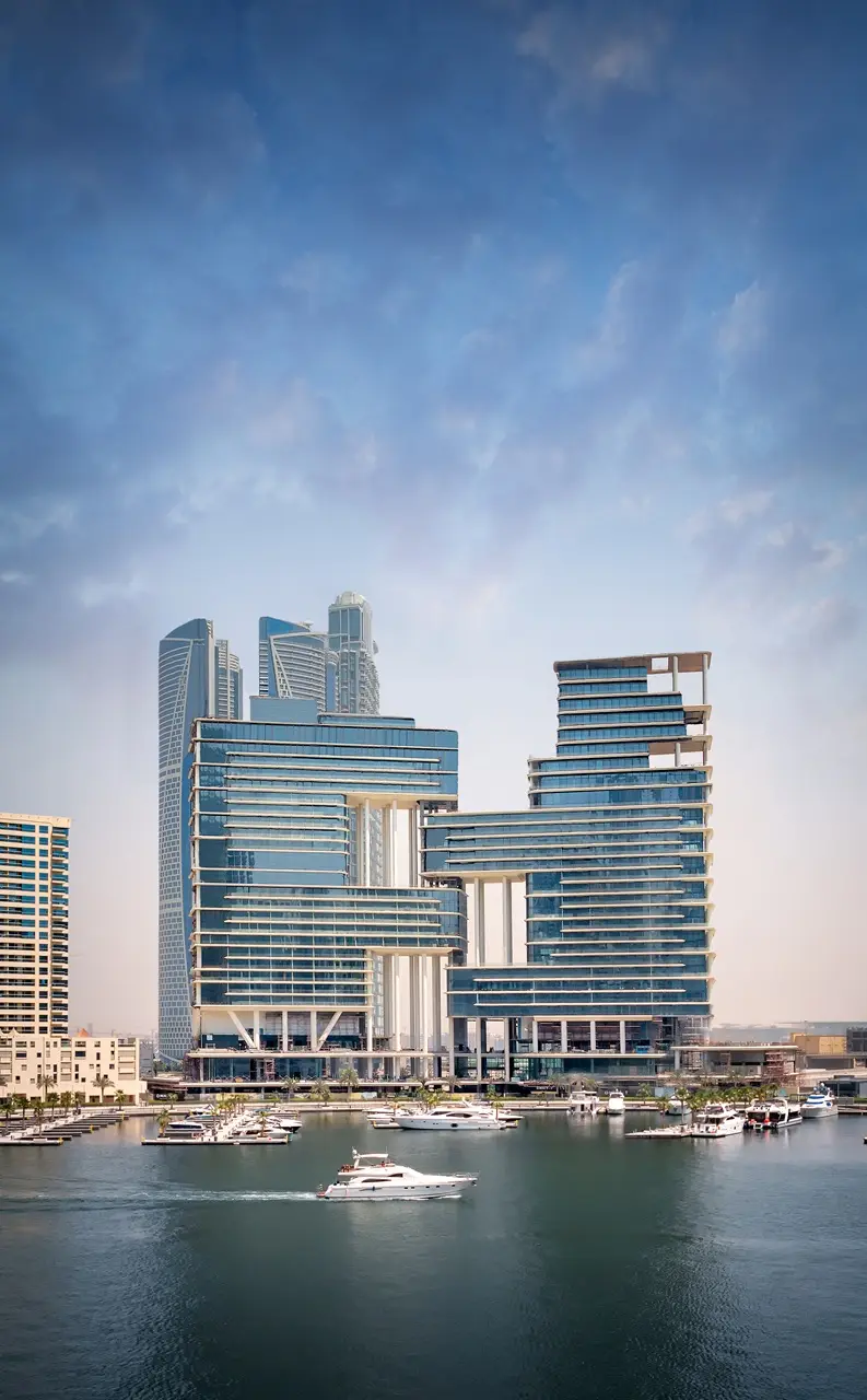 The Lana Residences Dorchester Collection by Omniyat waterfront towers with marina and yachts under clear blue sky in Dubai - Presented by Tohid Fetrat