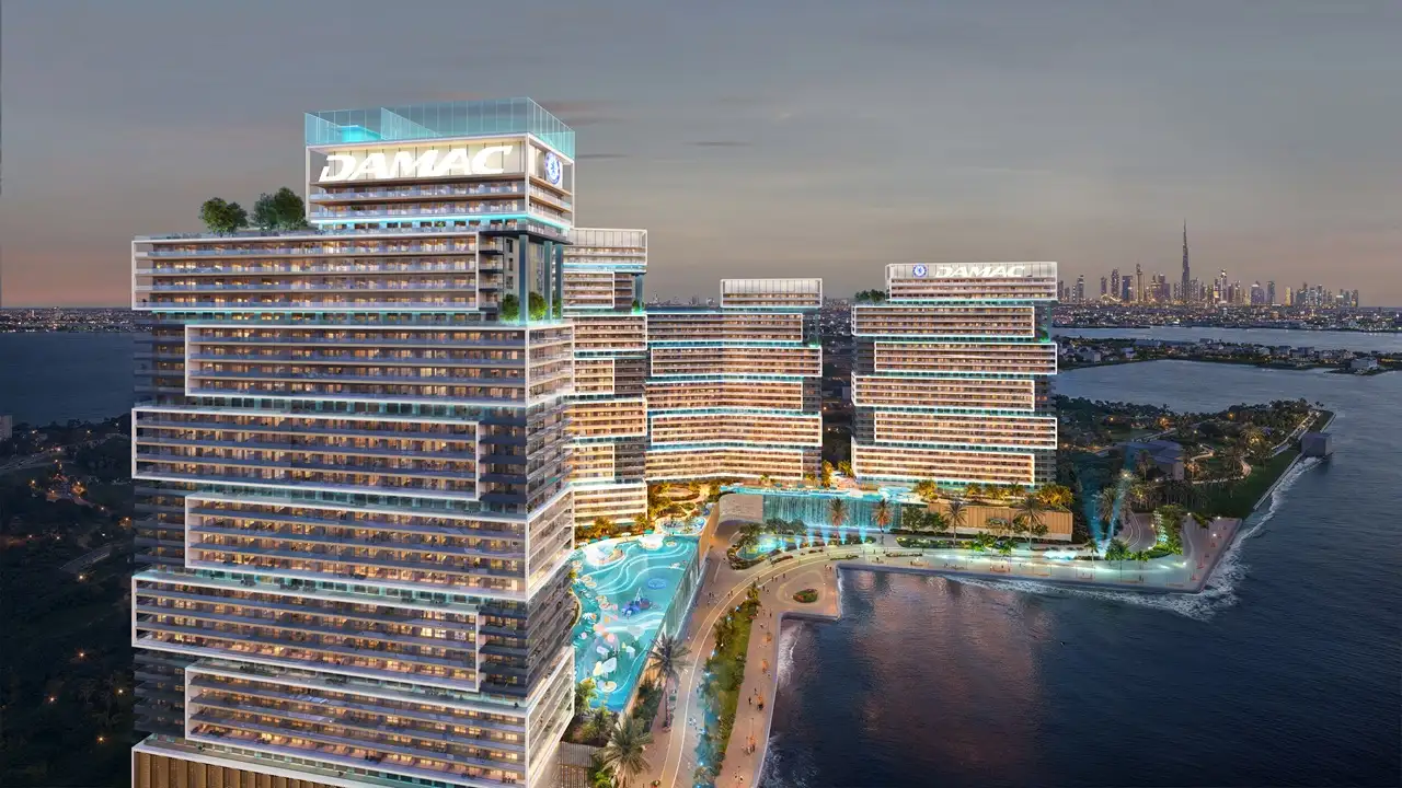 Chelsea Residences by DAMAC construction update showing waterfront development with illuminated buildings and lagoon style amenities in Dubai Presented by Tohid Fetrat