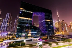 The Opus Residences by OMNIYAT illuminated night exterior with Burj Khalifa view in Dubai - Presented by Tohid Fetrat