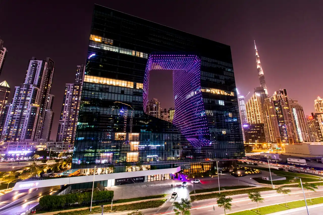 The Opus Residences by OMNIYAT illuminated night exterior with Burj Khalifa view in Dubai - Presented by Tohid Fetrat