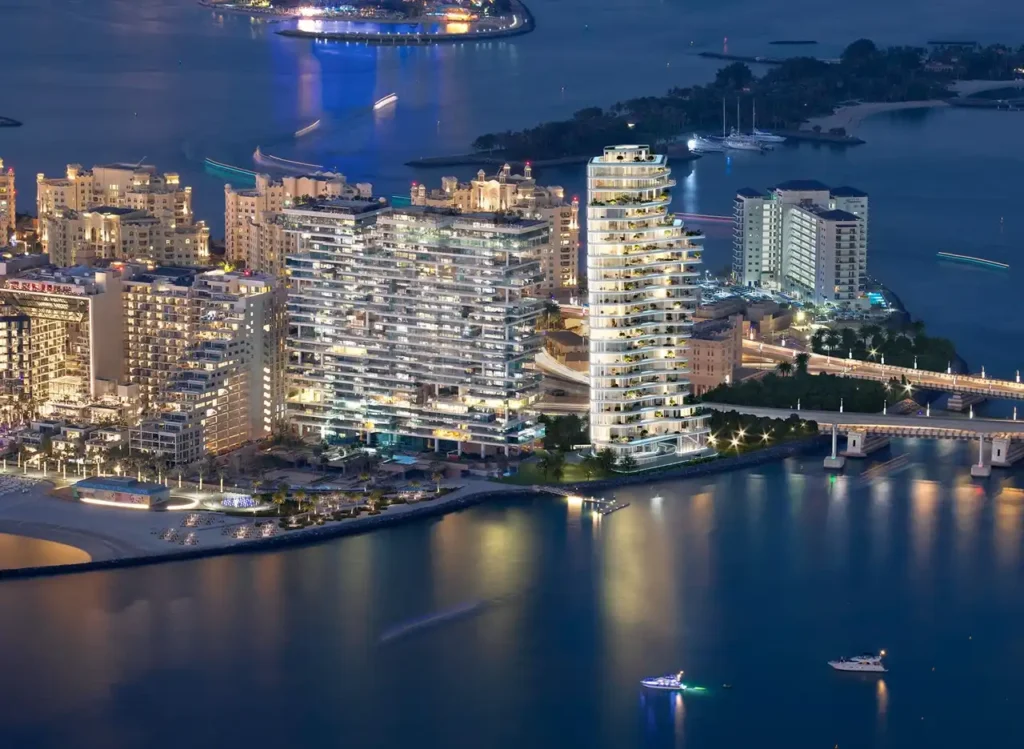 AVA at Palm Jumeirah, Dorchester Collection by OMNIYAT illuminated waterfront tower and surrounding coastal skyline at night in Dubai Presented by Tohid Fetrat